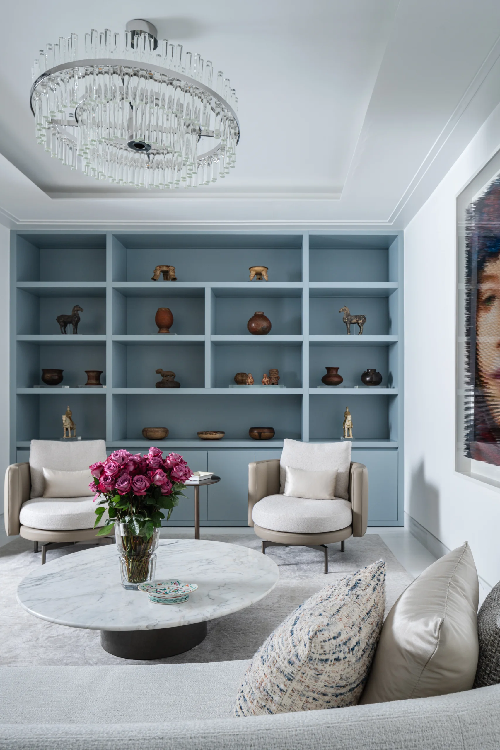 Sitting room with a powder-blue built-in cabinet displaying a curated collection of antique pottery and sculpture, Coco Plum Revival project by Dunagan Design.