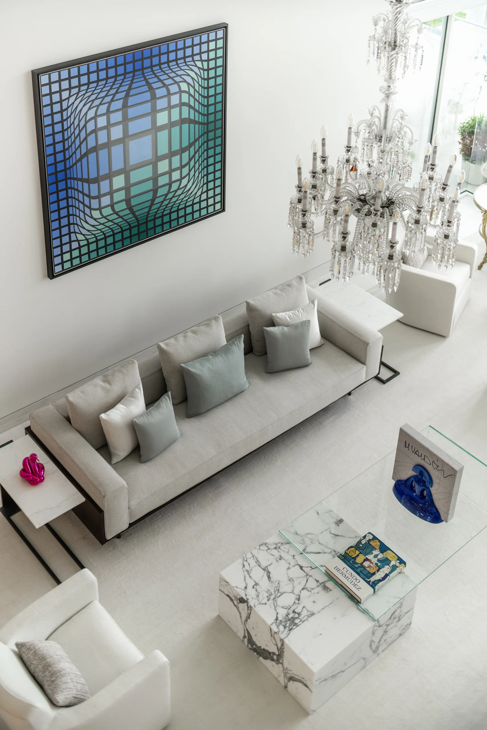 Living room detail with a crystal chandelier, op-art painting, and marble cocktail tables styled with art books and glass sculpture, Coco Plum Revival project by Dunagan Design.