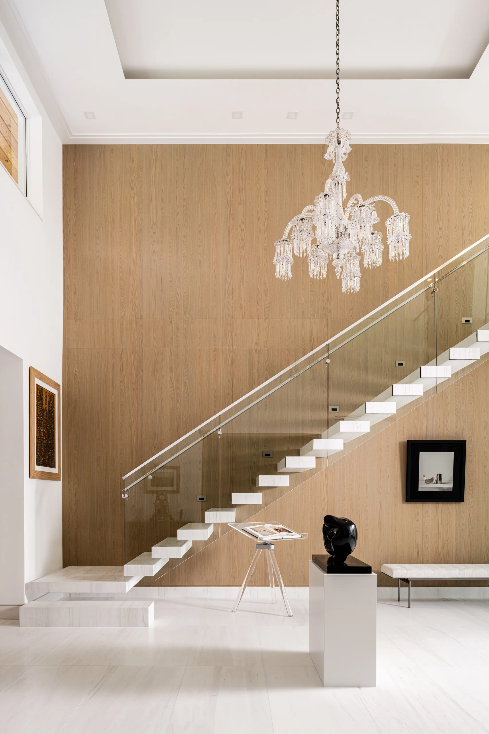 Entry foyer with a floating marble staircase, glass railing, crystal chandelier, and sculptural art display, Coco Plum Revival project by Dunagan Design.