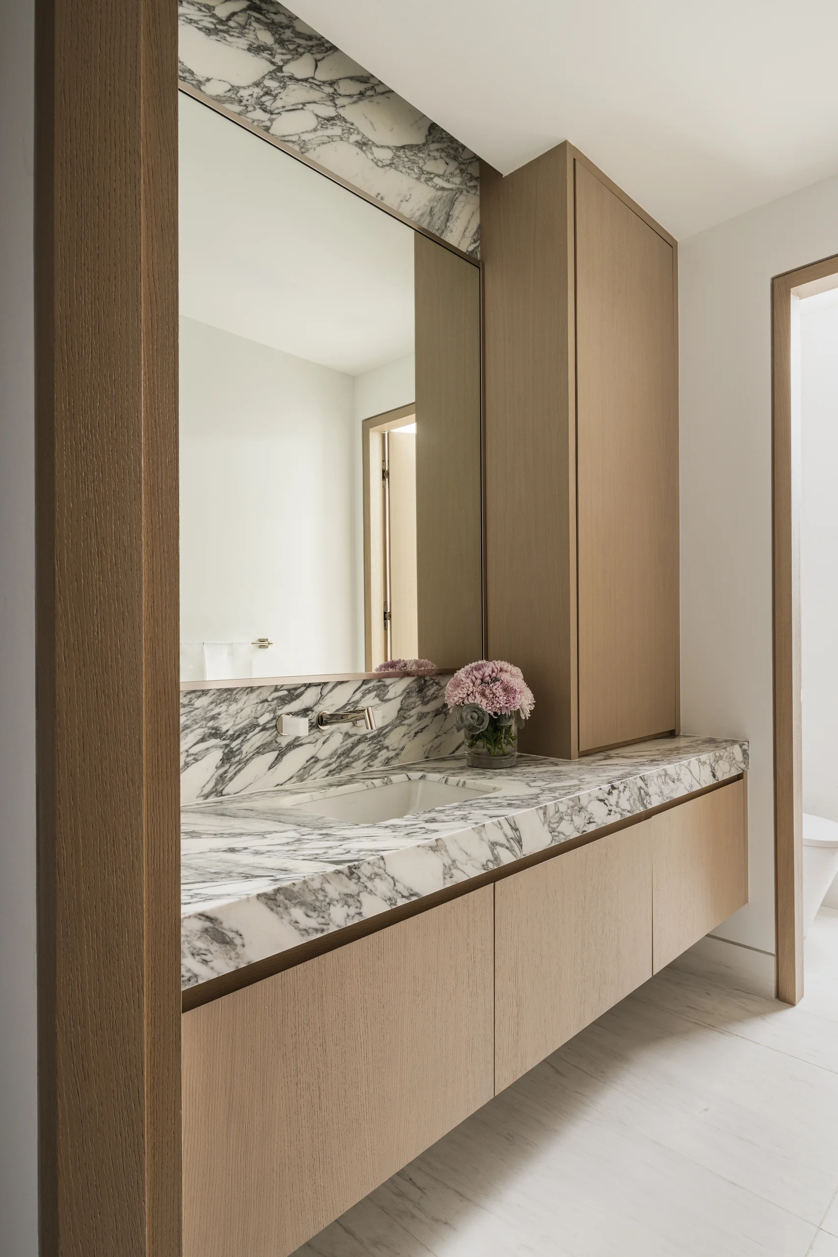 Bathroom vanity with a dramatic marble slab backsplash and floating oak cabinetry, Coco Plum Revival project by Dunagan Design.