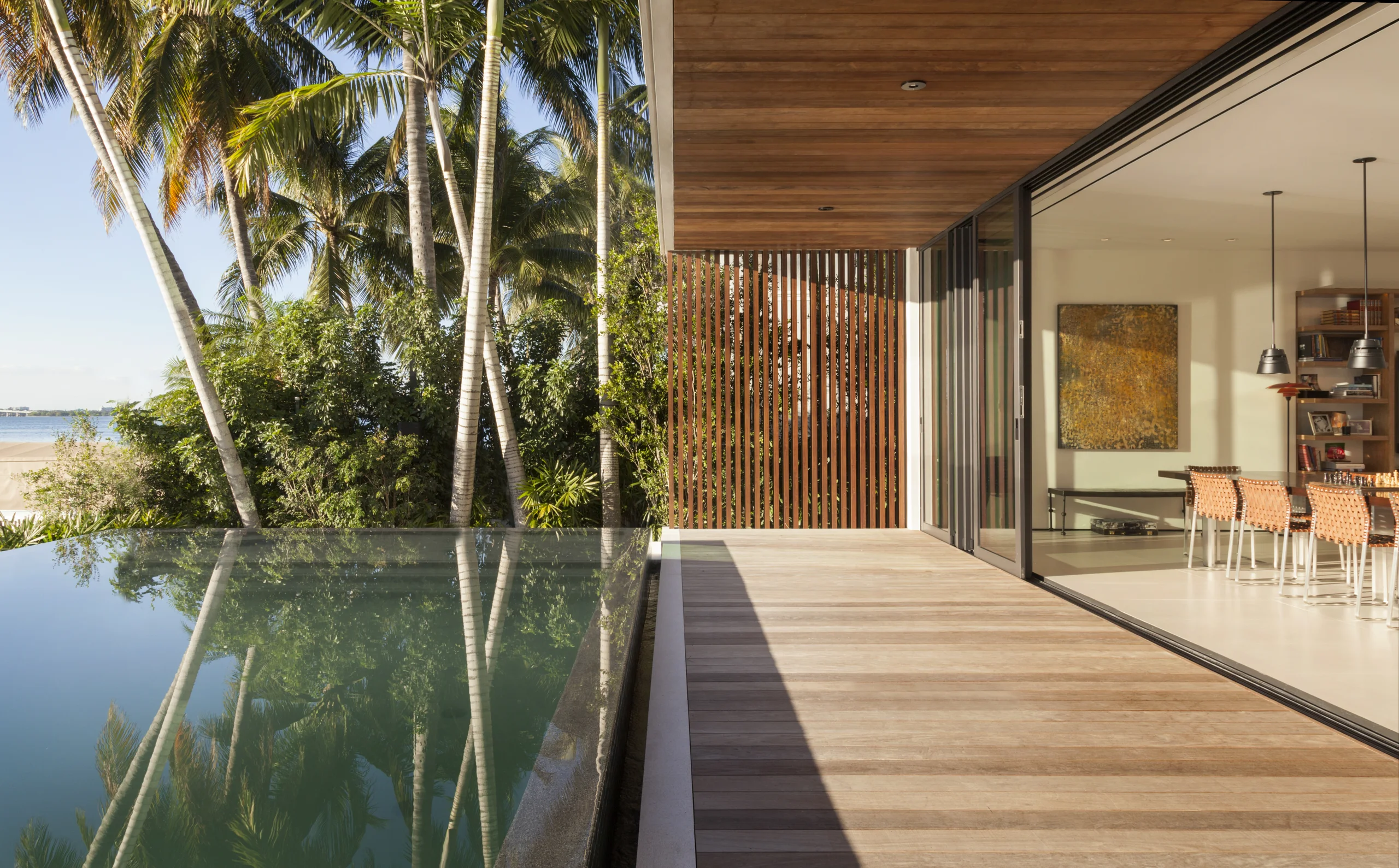 Pool deck view past palm trees into the open dining room, Bayside Modern project by Dunagan Design.