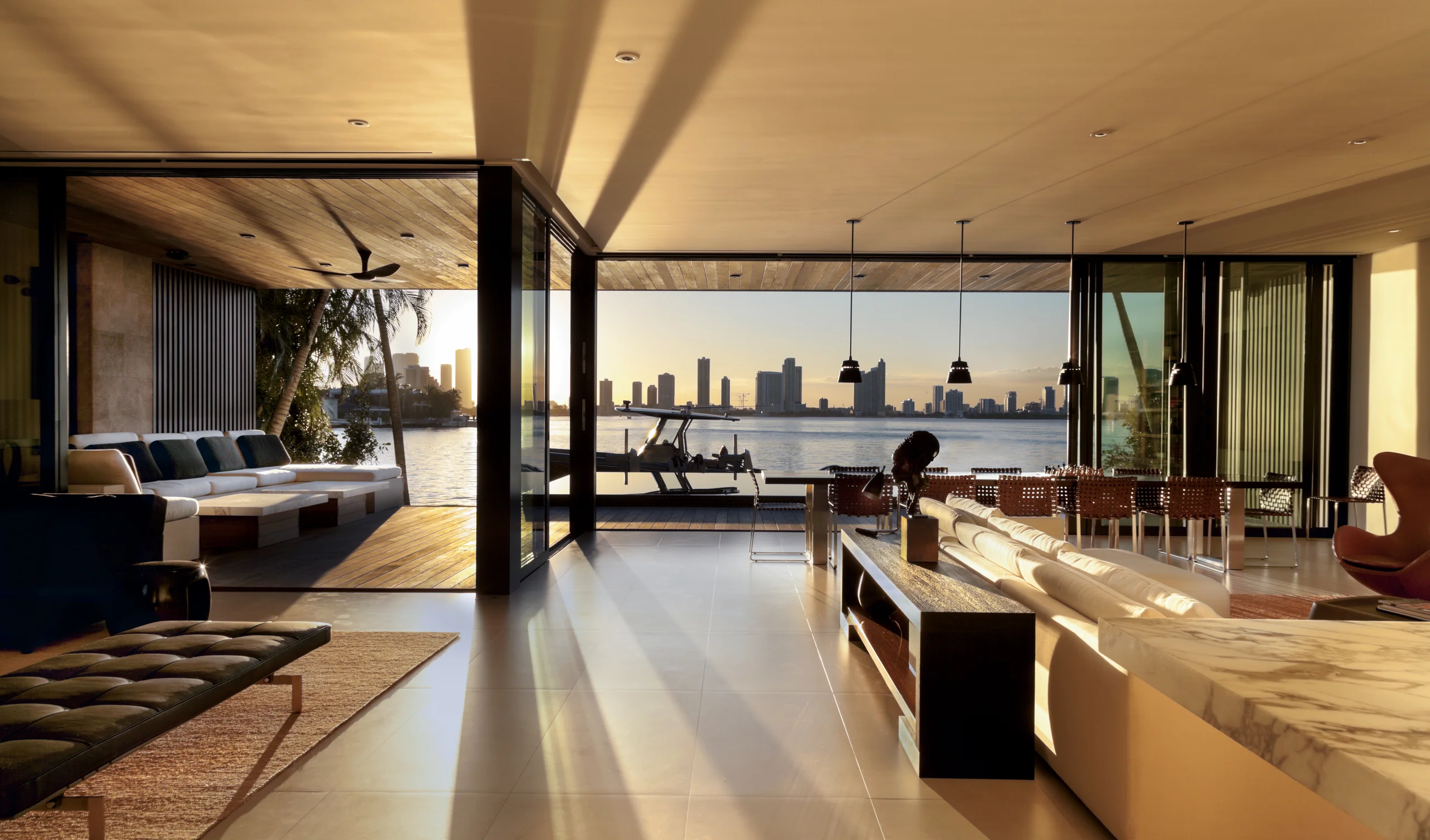 Open-air living and dining room at golden hour with walls of glass sliding open to the bay, Bayside Modern project by Dunagan Design.