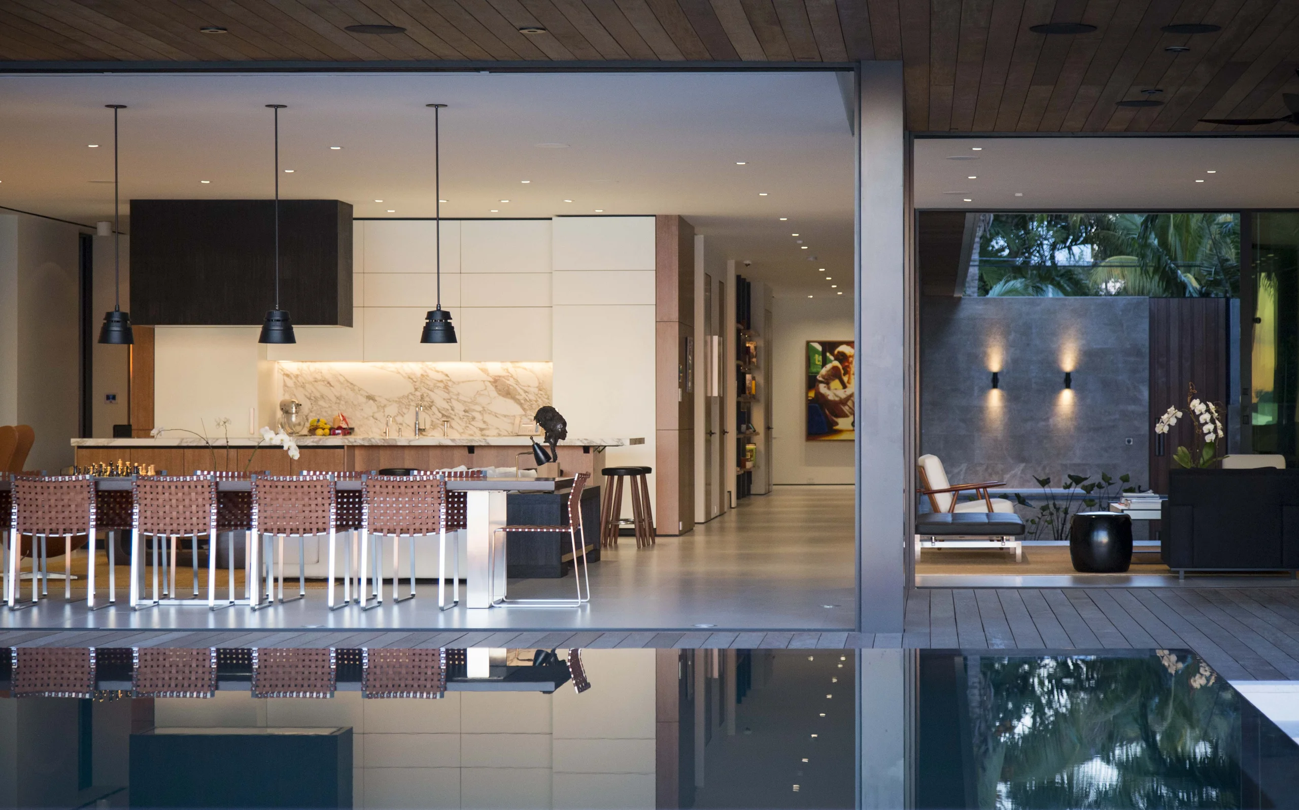 View from the pool deck into the open kitchen with woven leather counter stools and a marble backsplash, Bayside Modern project by Dunagan Design.