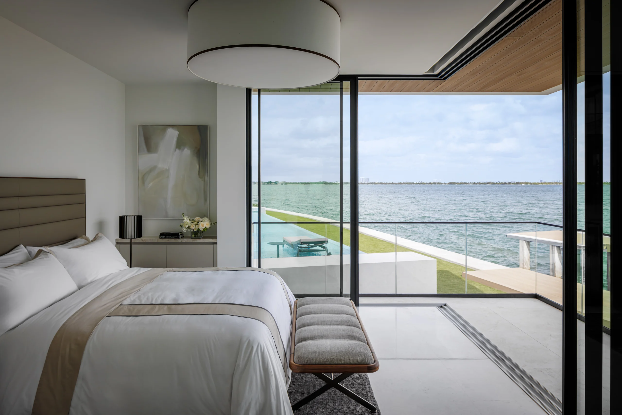 Primary bedroom with a channel-tufted headboard and floor-to-ceiling glass opening to a private waterfront balcony, San Marino Gallery project by Dunagan Design.