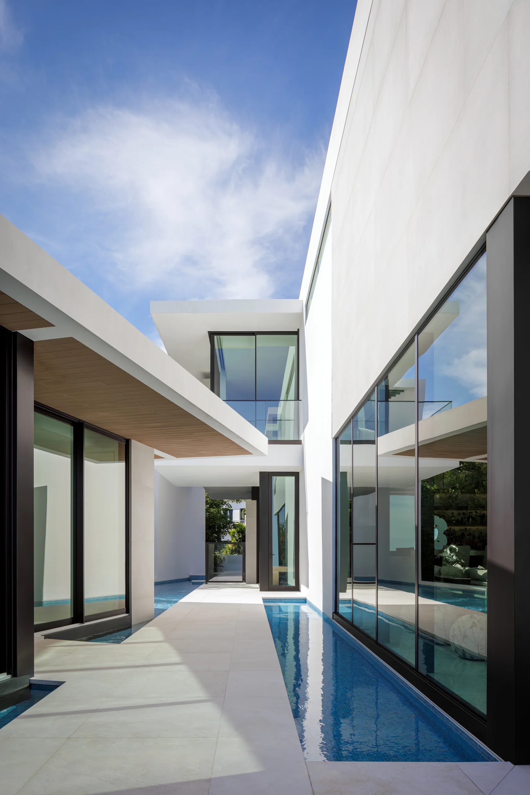 Narrow reflecting pool running alongside glass-walled interiors, framed by the home's modern white facade, San Marino Gallery project by Dunagan Design.