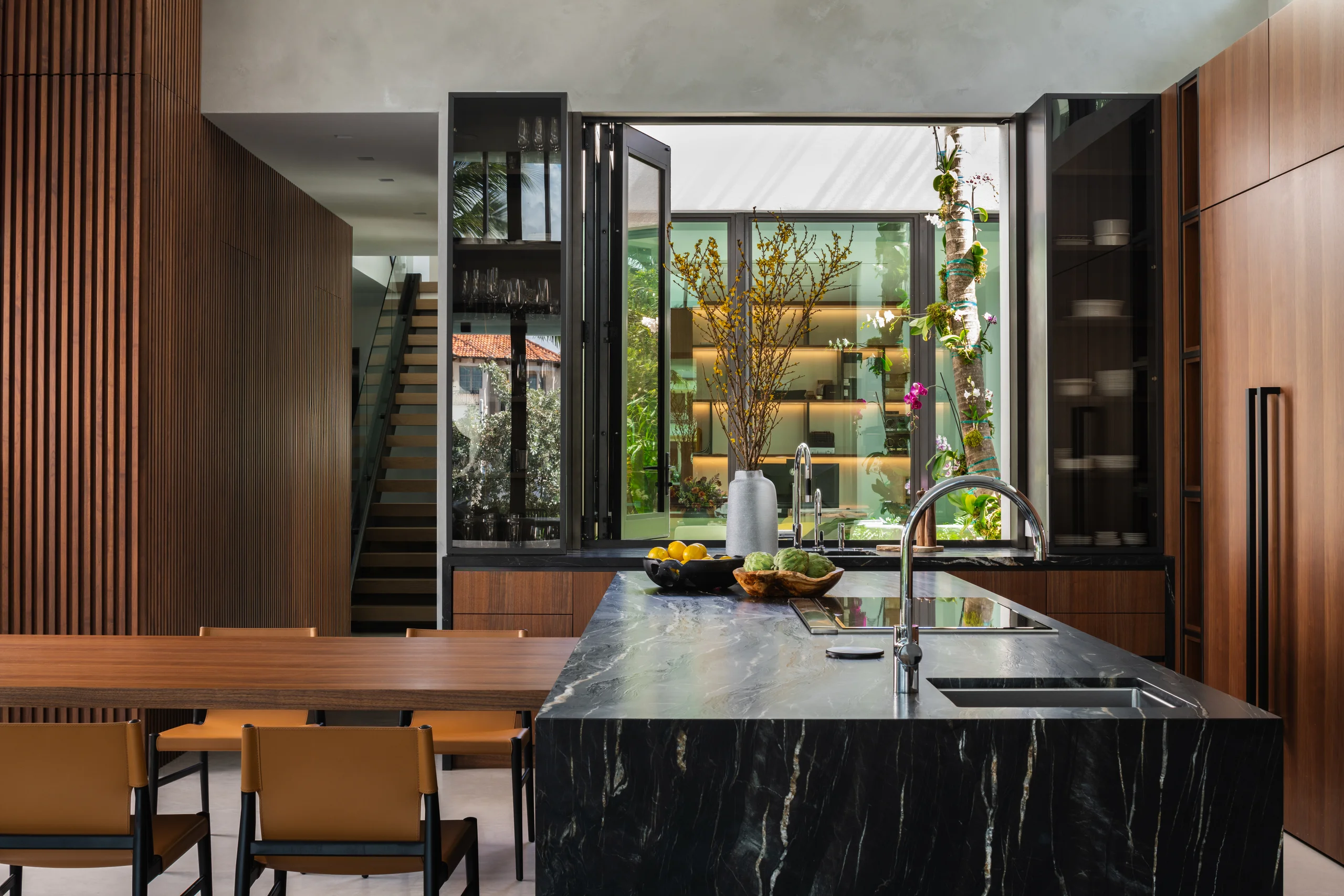 Kitchen island in exotic black stone facing a folding glass window onto an interior courtyard, Spanish River Modern project by Dunagan Design.