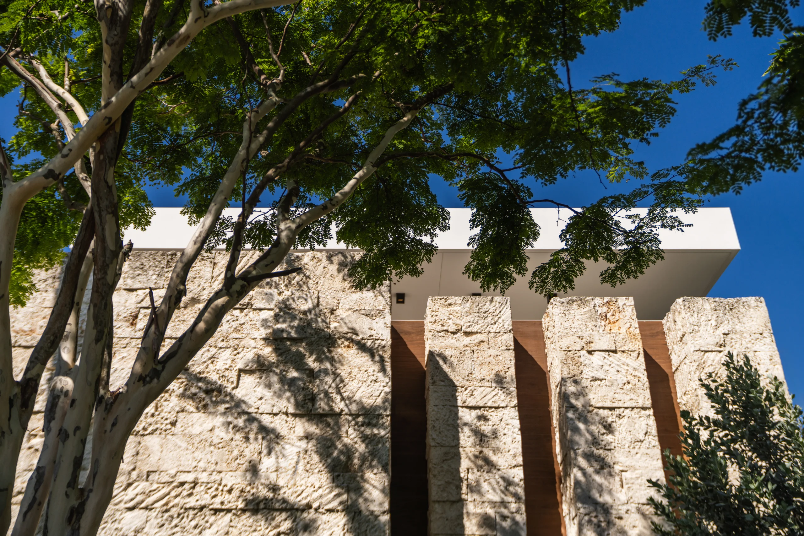 Exterior detail of rough-hewn coral stone piers beneath a cantilevered roofline, Spanish River Modern project by Dunagan Design.