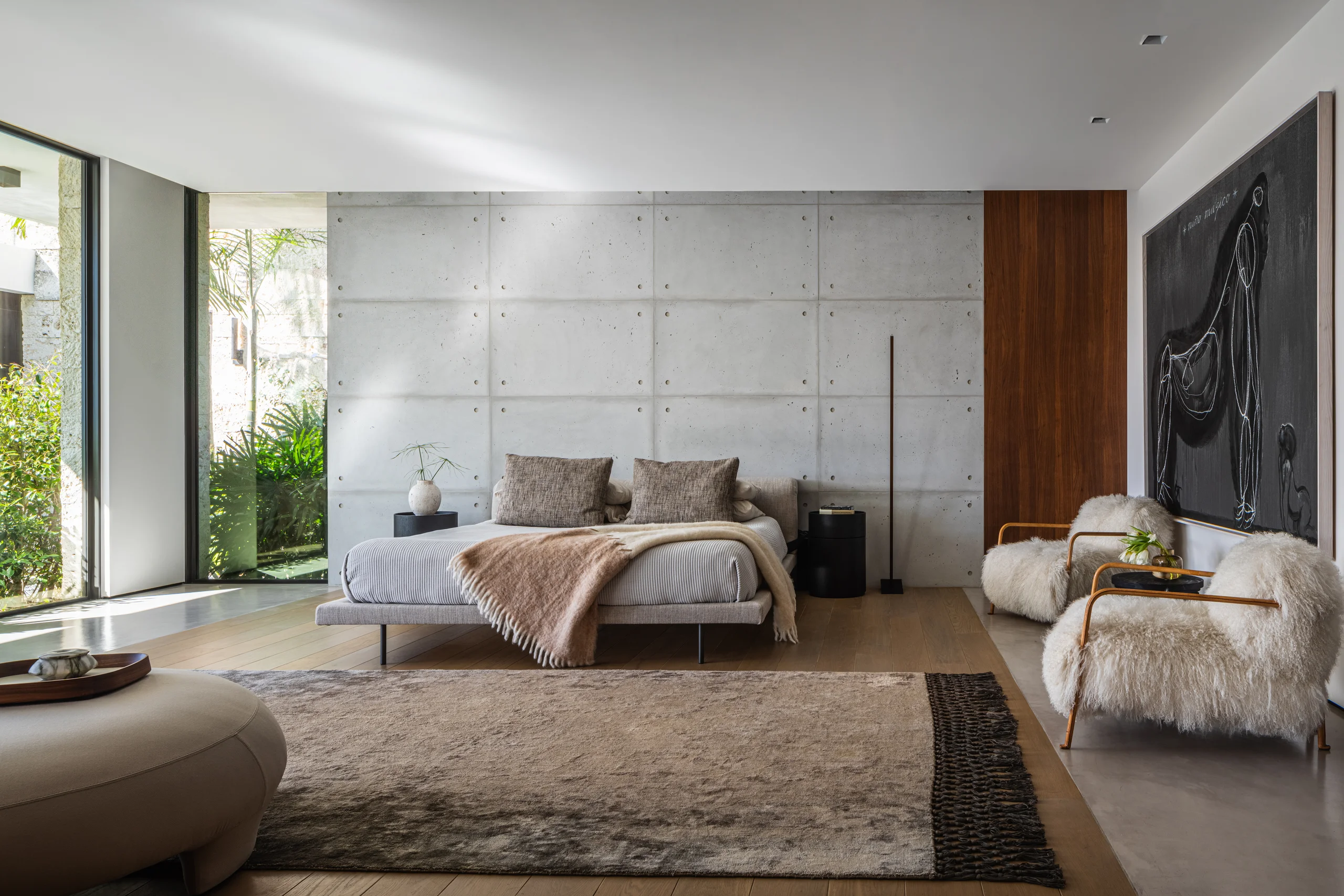 Primary bedroom with a board-formed concrete accent wall and shaggy lambswool lounge chairs, Spanish River Modern project by Dunagan Design.