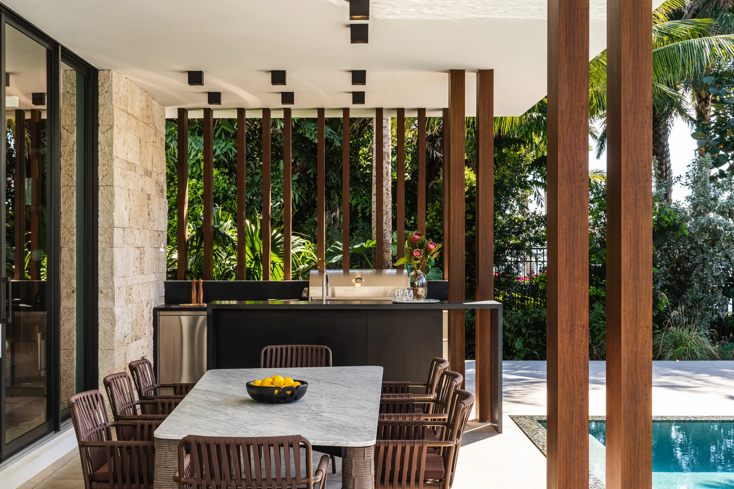 Covered outdoor dining and summer kitchen framed by a wood-fin screen and tropical landscaping, Spanish River Modern project by Dunagan Design.