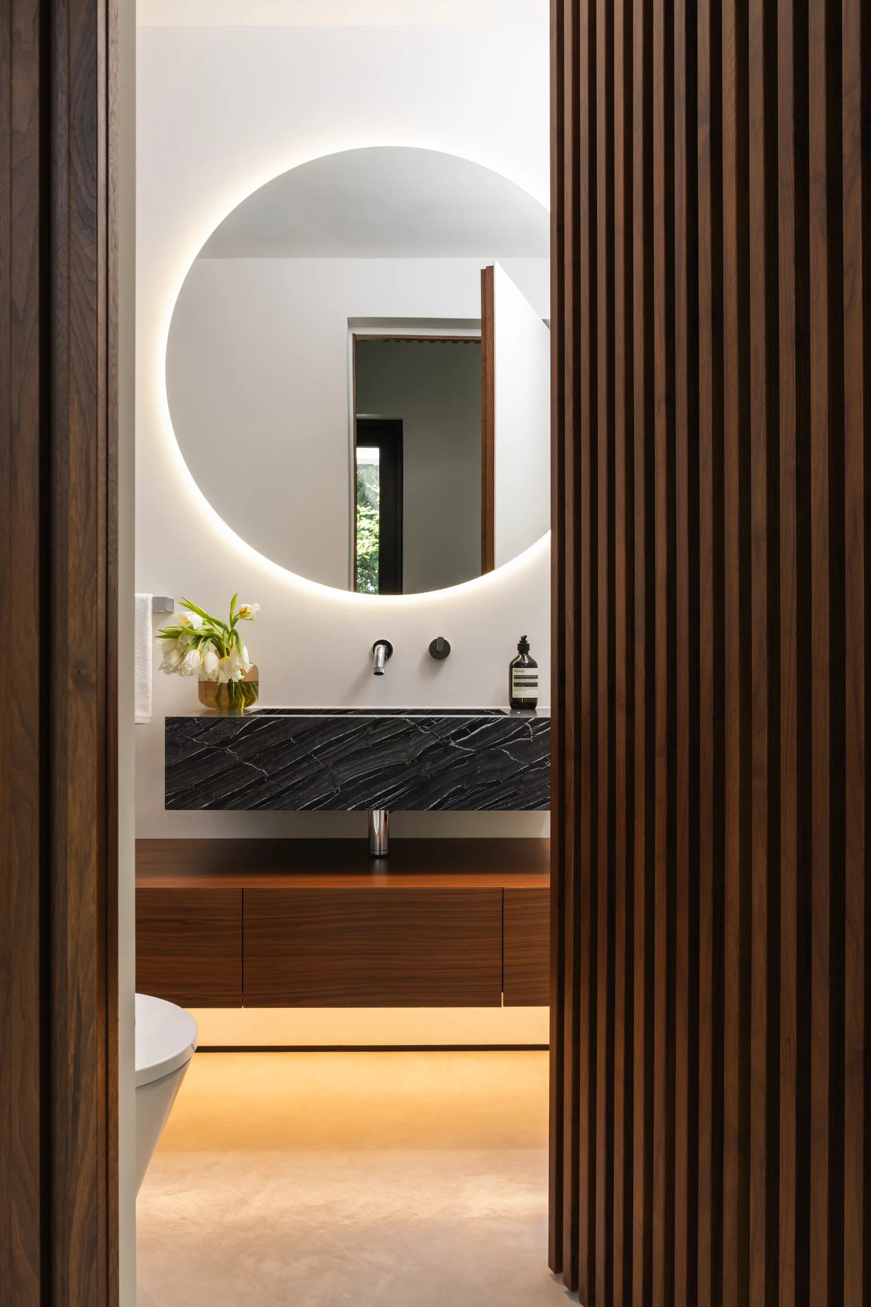 Powder room with a backlit circular mirror and a floating black stone vanity, Spanish River Modern project by Dunagan Design.