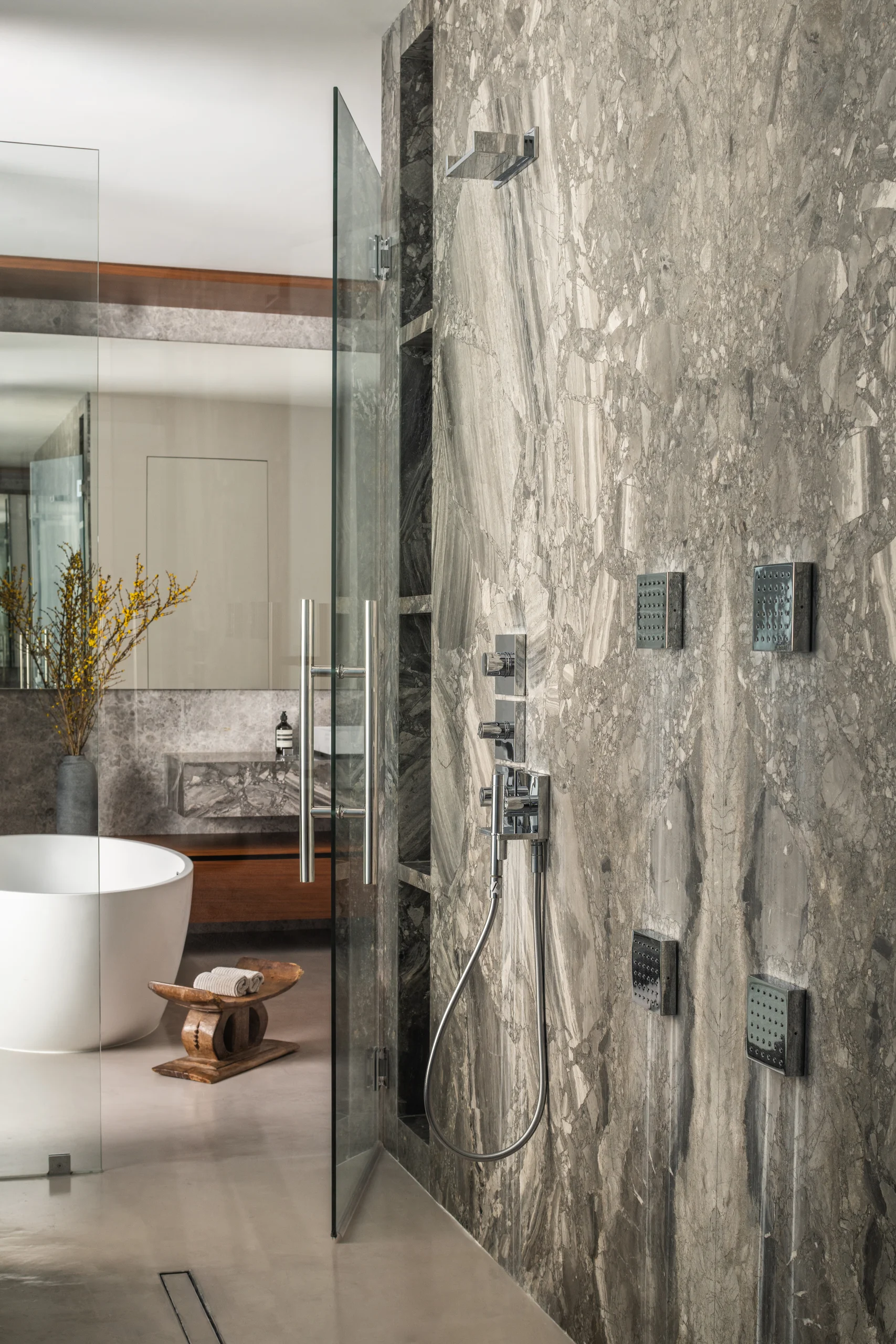 Primary bathroom shower with a fossil-stone slab wall and integrated body jets, Spanish River Modern project by Dunagan Design.