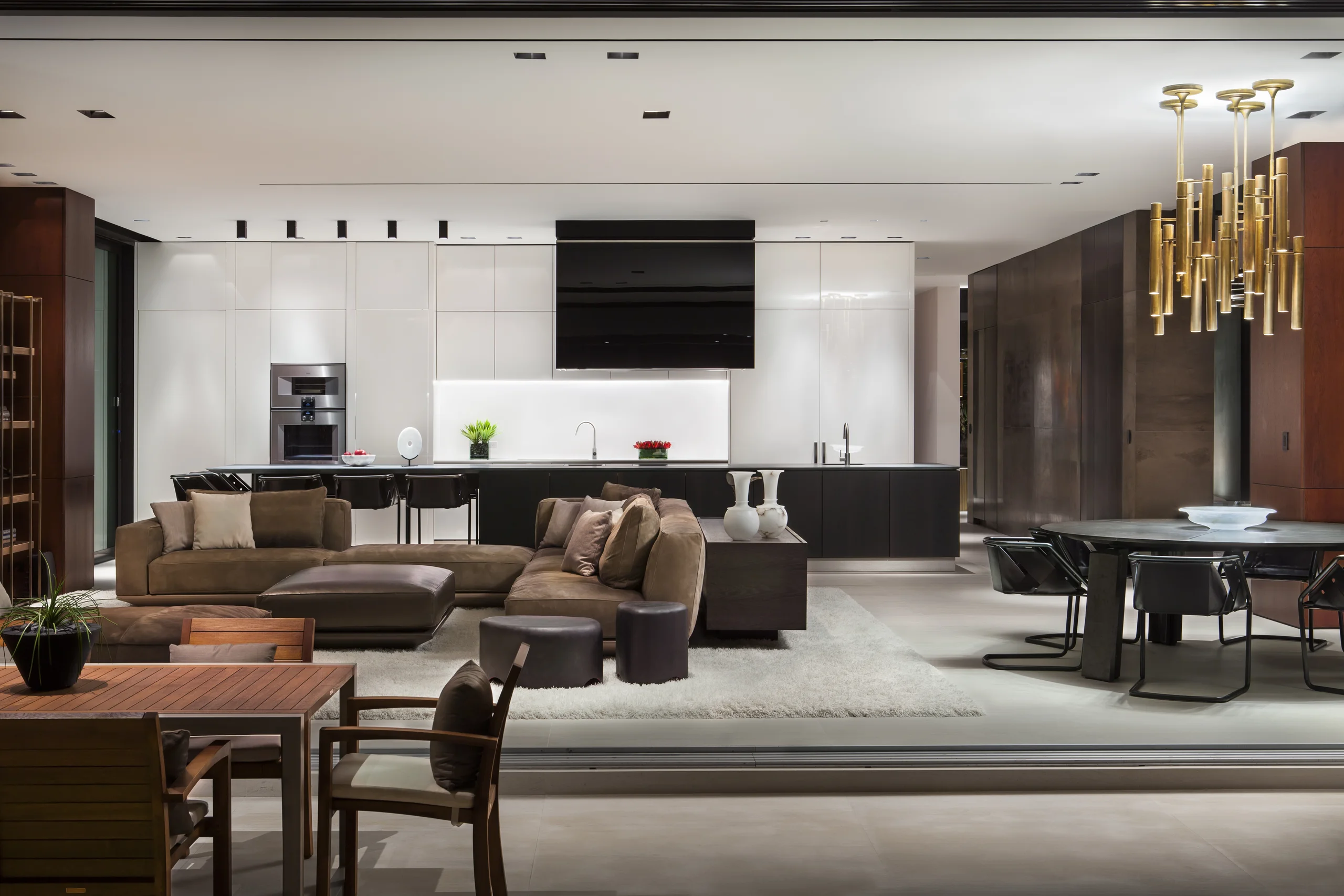 Open living, kitchen, and dining area with a gold bamboo-style chandelier and a leather sectional, DiLido Modern project by Dunagan Design.