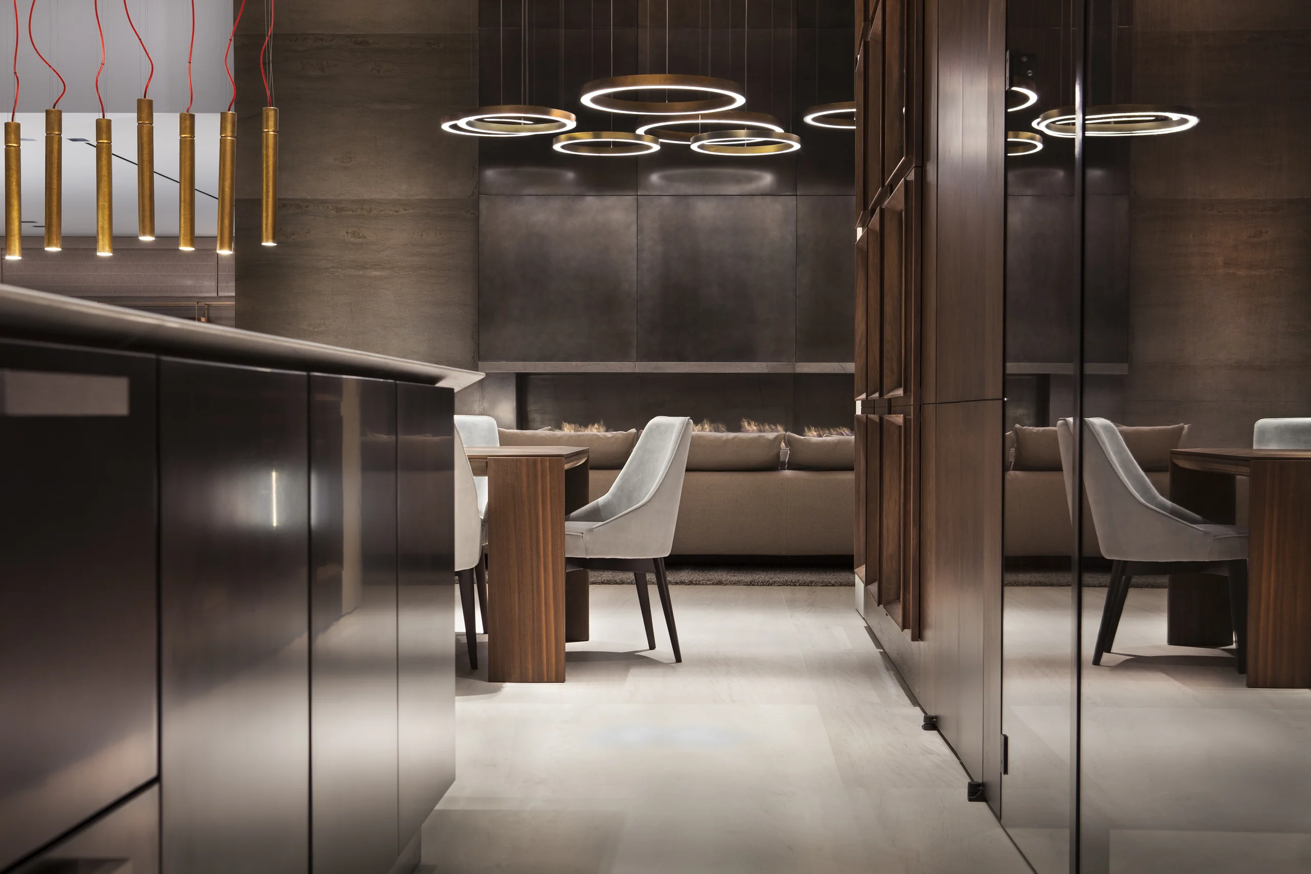Living and dining area with a sculptural gold ring pendant cluster and a mirrored dark cabinetry wall, DiLido Modern project by Dunagan Design.