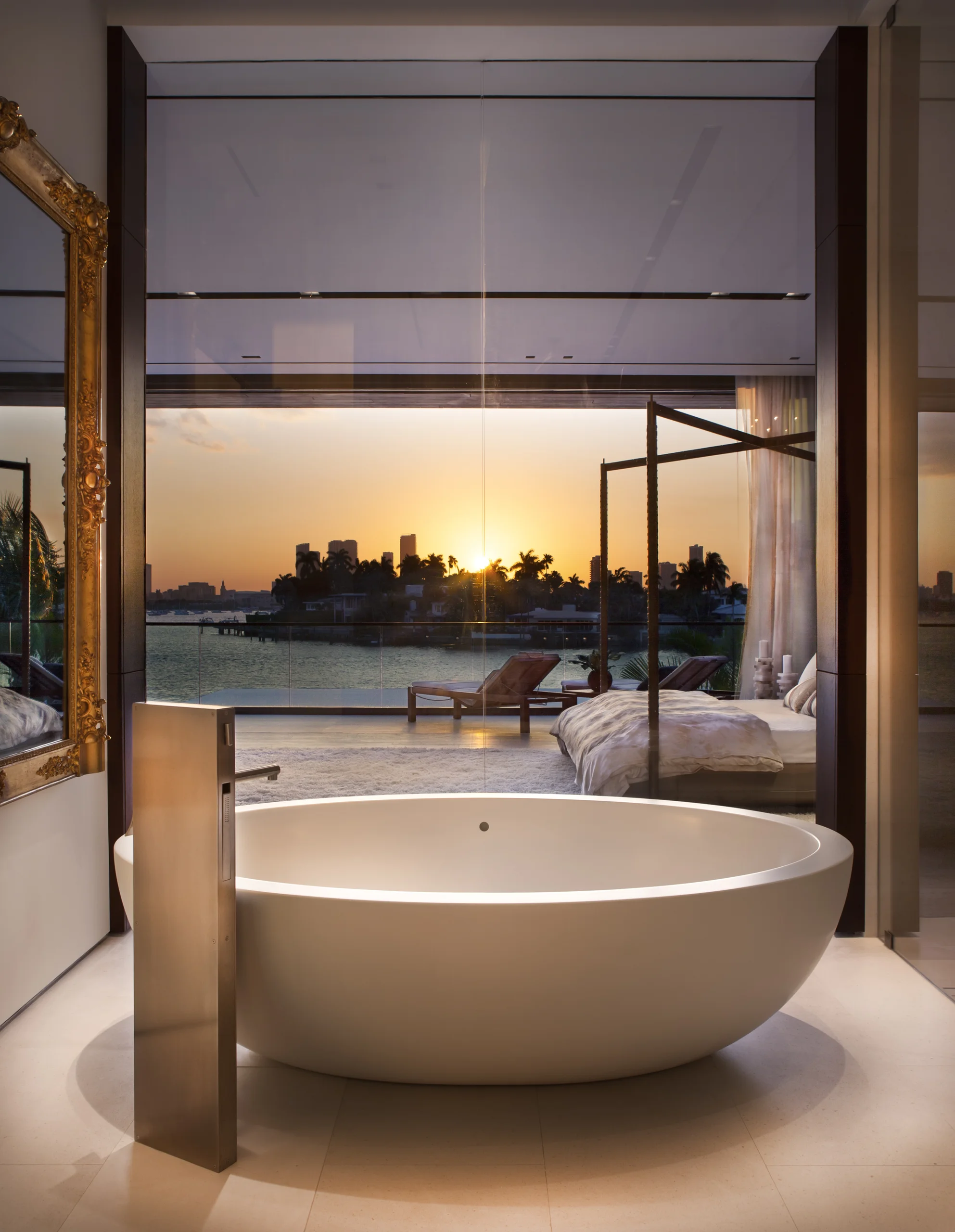 Primary bathroom with a sculptural oval soaking tub facing the bedroom and a sunset skyline view, DiLido Modern project by Dunagan Design.