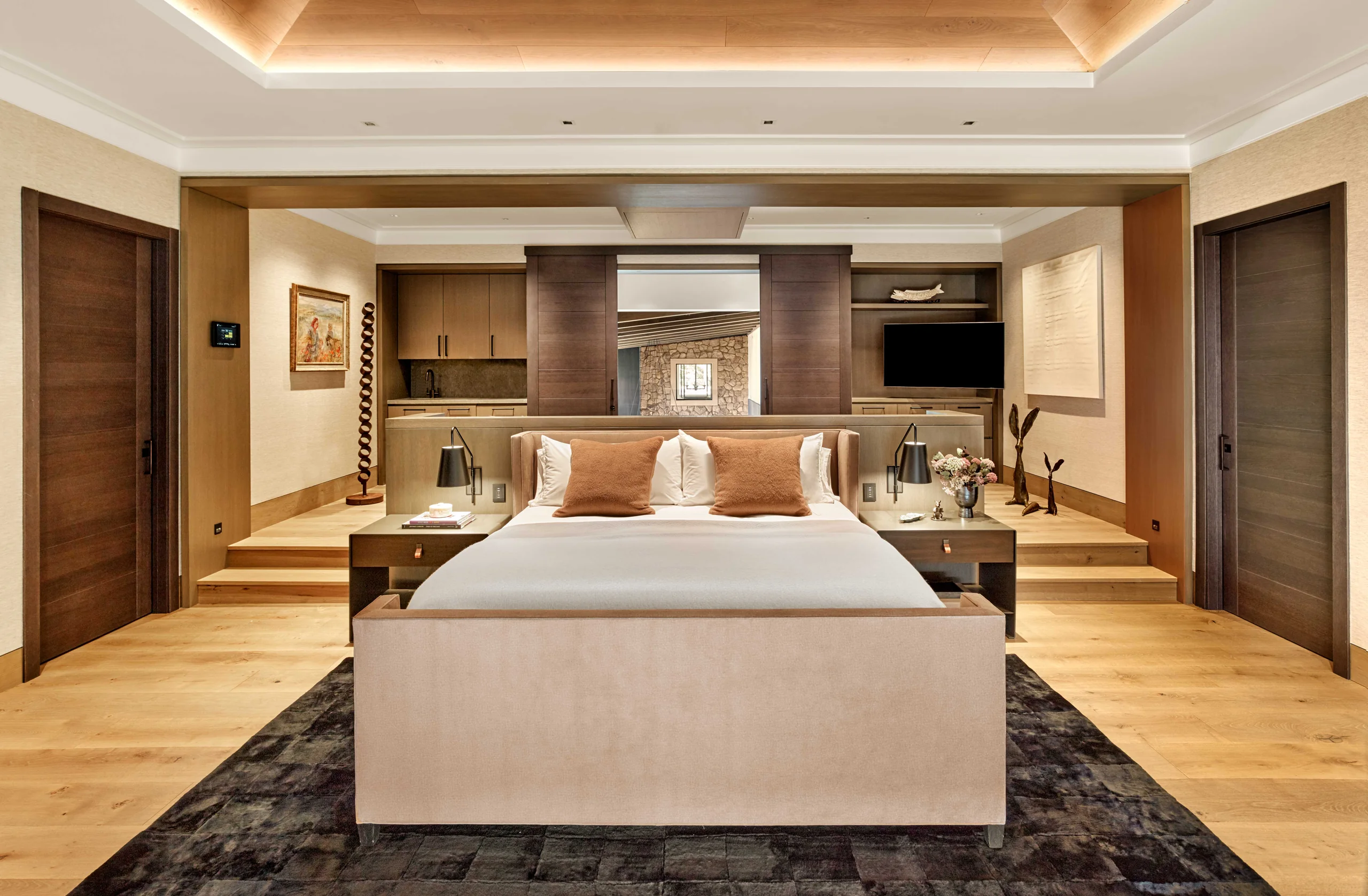 Primary bedroom with an upholstered bed, a wood-lined tray ceiling with cove lighting, a kitchenette niche, and a dark patchwork rug, Napa Valley Estate project by Dunagan Design.