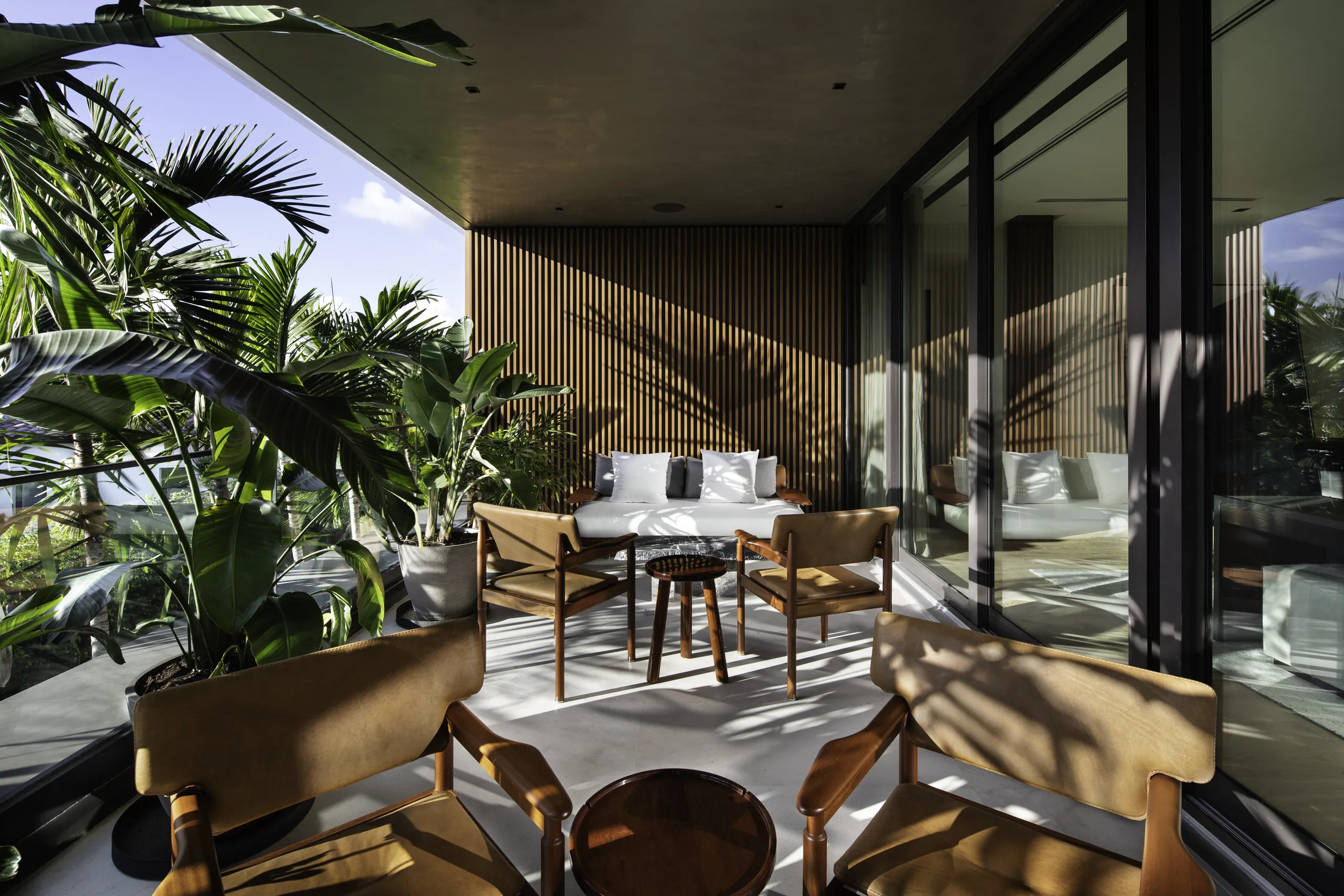 Covered balcony lounge with wood-slat walls, camel leather chairs, and tropical plantings, Star Island Waterfront project by Dunagan Design.