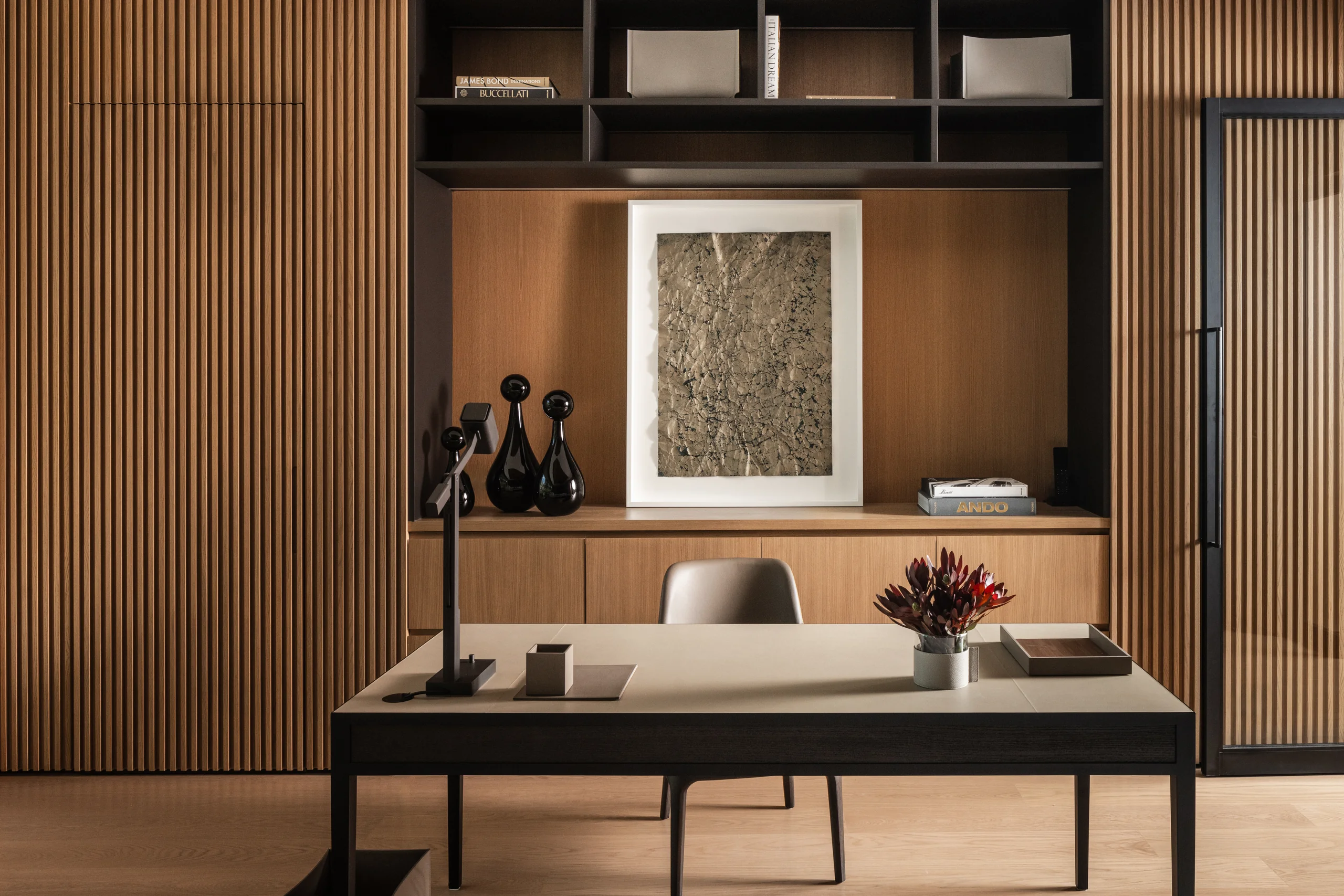 Home office with oak slat paneling, a stone-topped desk with a leather chair, black built-in shelving, and a framed textured artwork, Sunset Island House project by Dunagan Design.