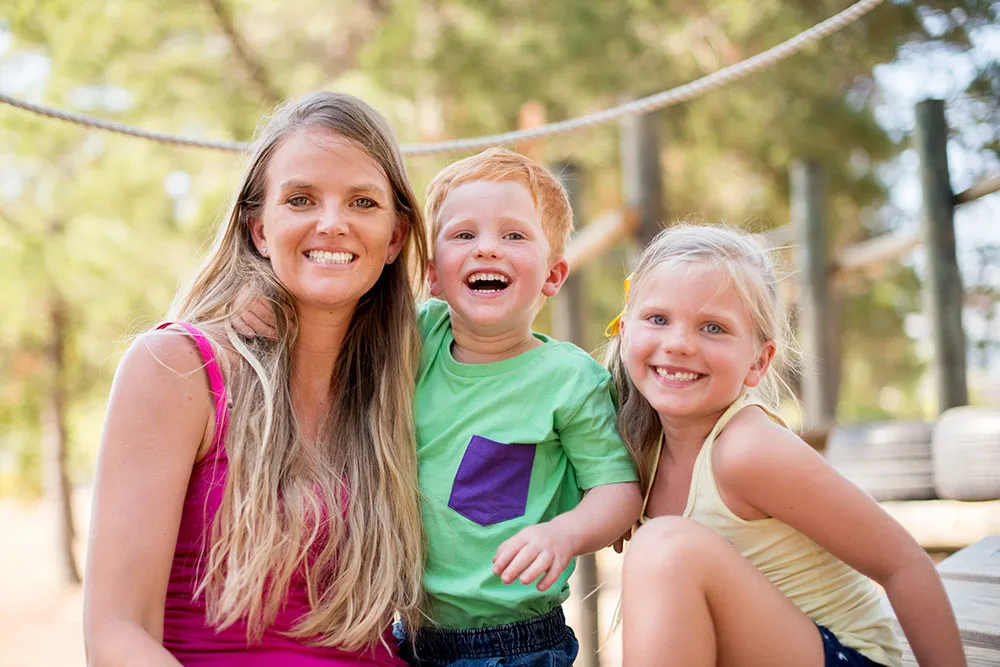 Mum with her two young children smiling in a playground