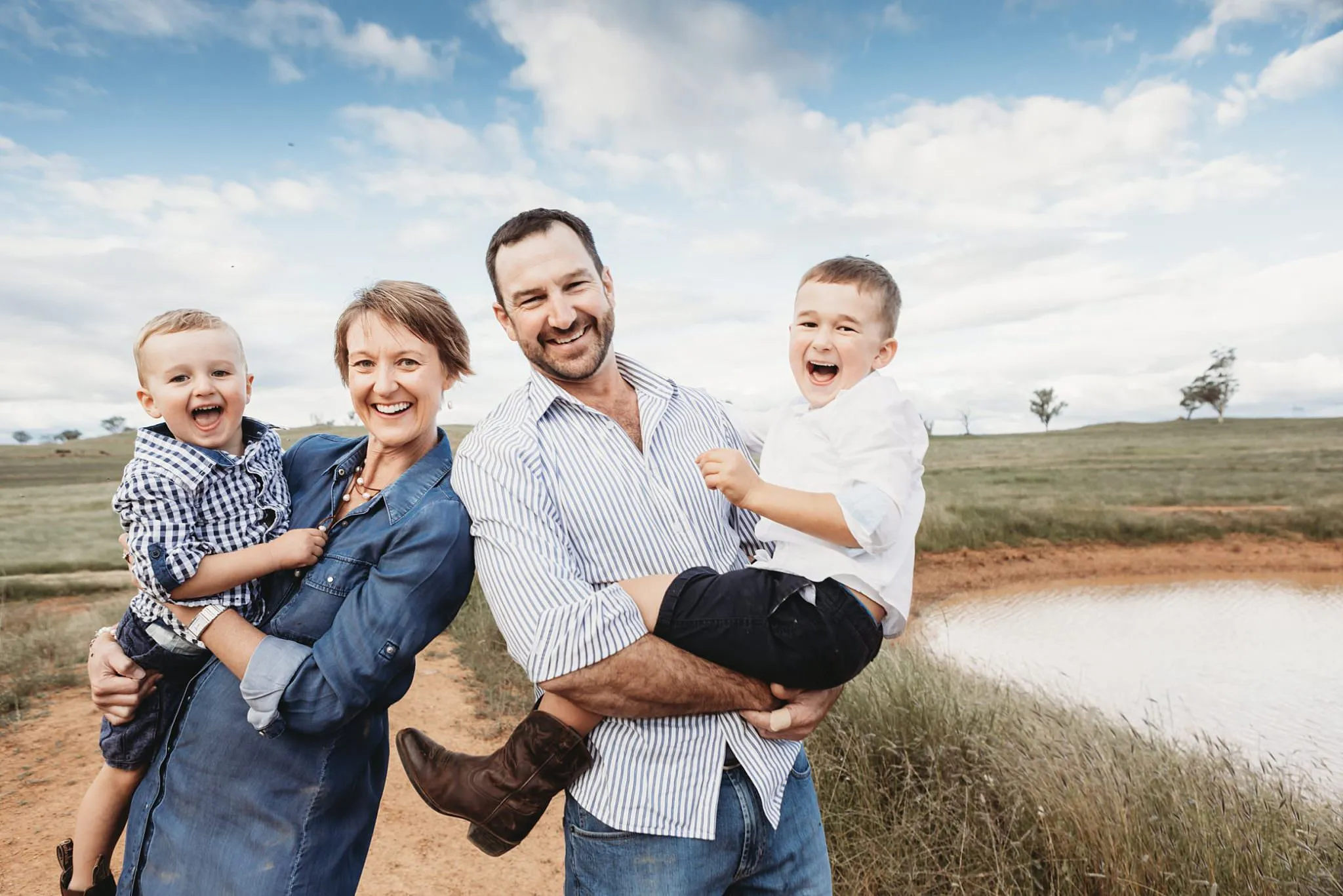 Family with two young boys laughing in a paddock beside a farm dam near Tamworth