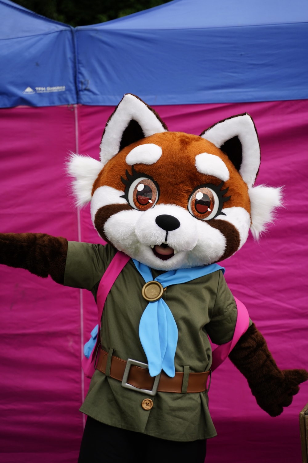 Maple is looking at the camera, with her arms held out playfully. A pink and blue gazebo is behind her.