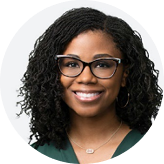 Smiling woman with curly hair and glasses wearing a green top and hoop earrings.