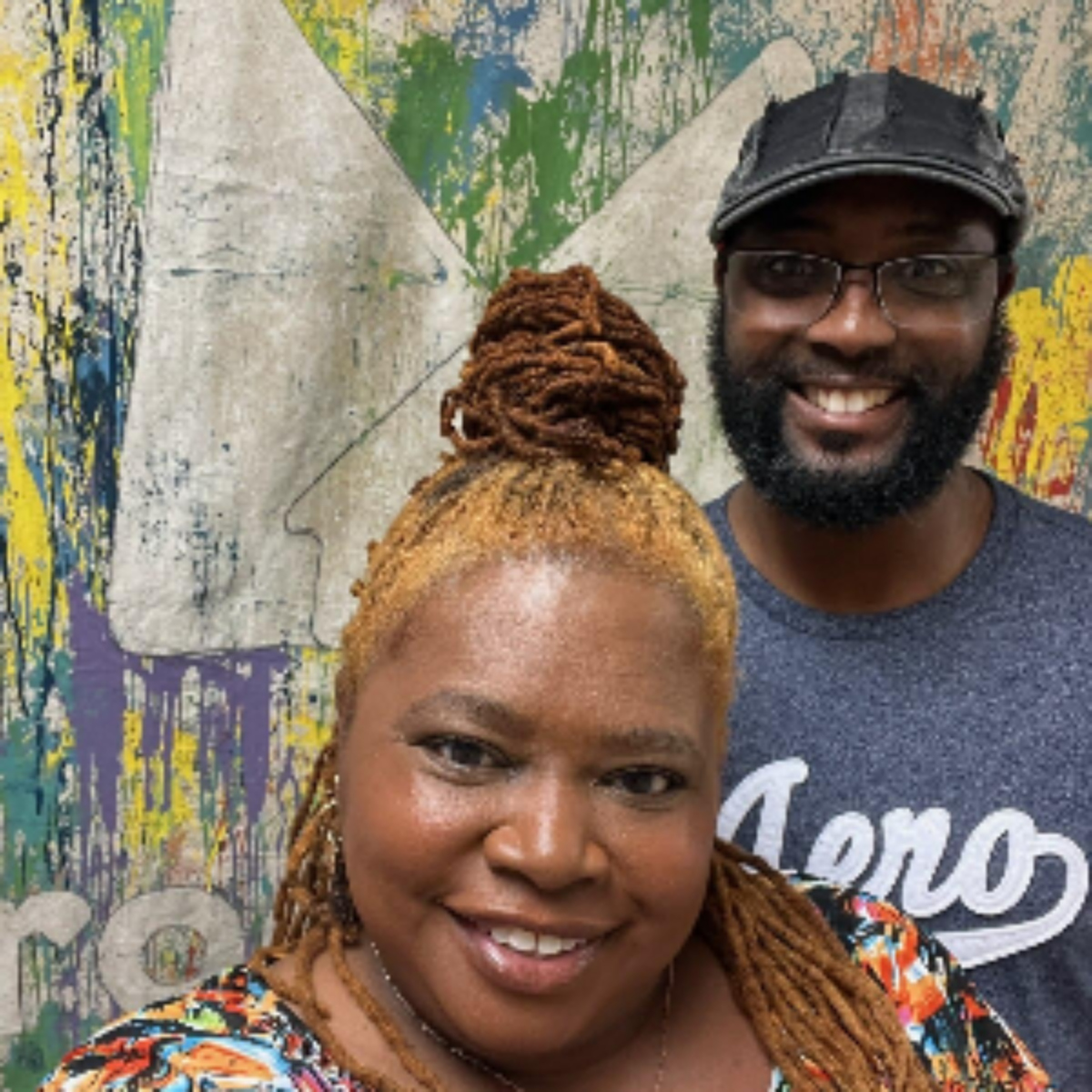 Smiling couple standing in front of a colorful textured wall with abstract patterns.