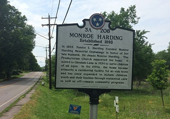 Historical roadside marker detailing Monroe Harding Memorial Orphanage established in 1893, located by a street with trees and grass.