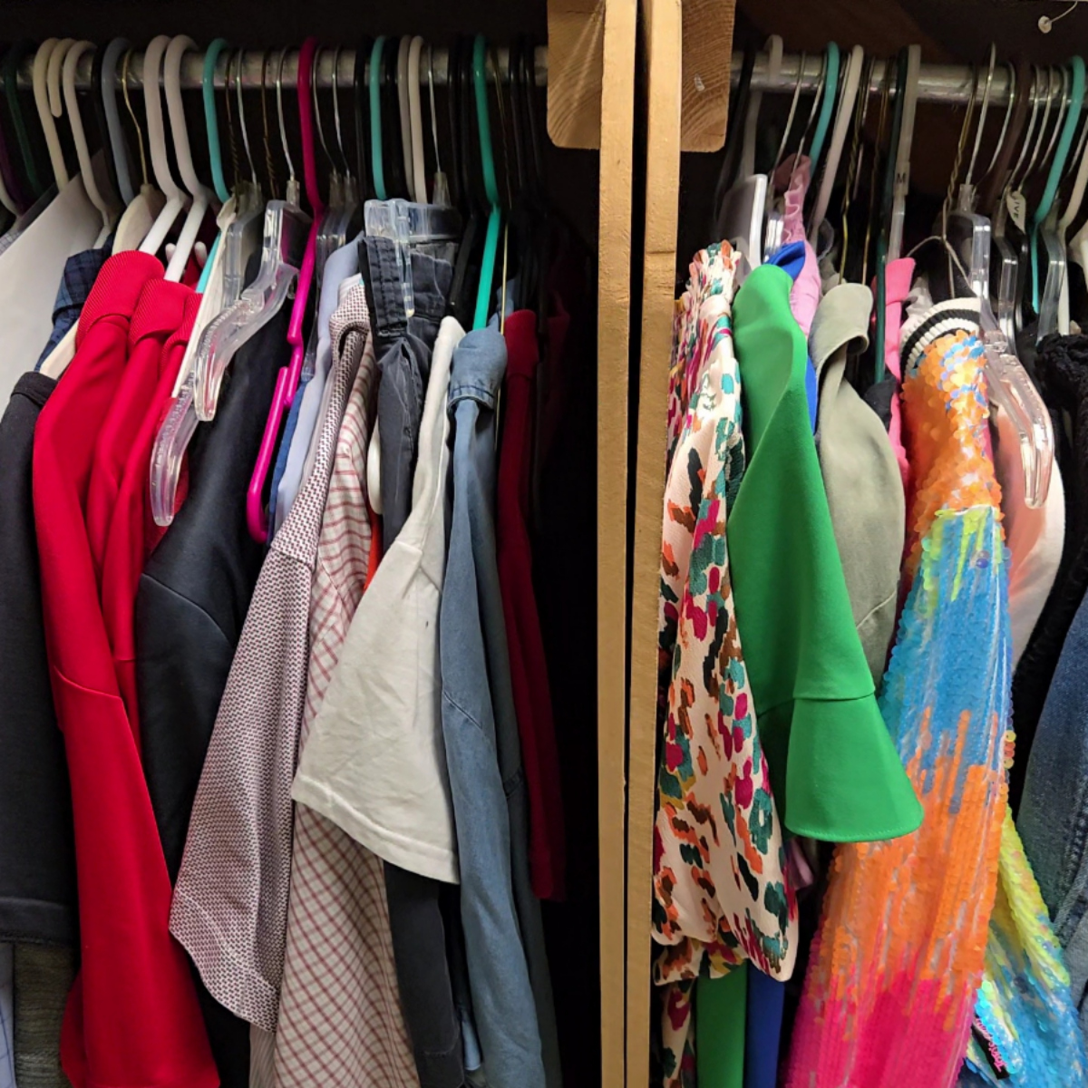 Closet with assorted clothes hanging on hangers, including red sweaters, patterned shirts, solid color tops, a green garment, and a colorful sequined dress.