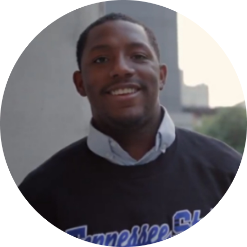 Smiling man wearing a black Tennessee State sweatshirt with a cityscape in the background.