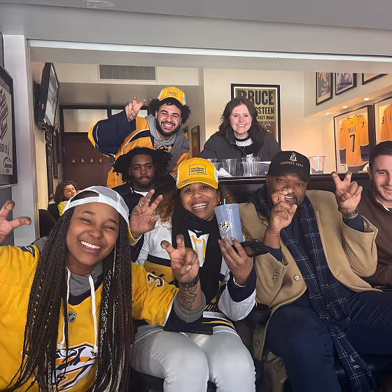 Group of six people wearing sports gear smiling and making peace signs indoors.