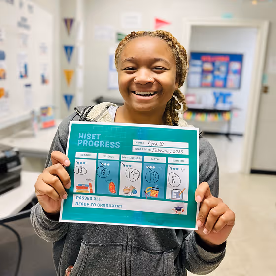 Smiling young woman holding a certificate showing HiSET progress and readiness to graduate.