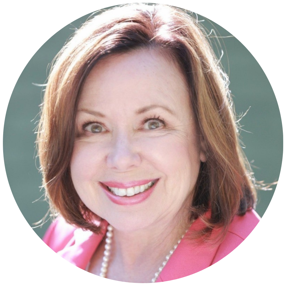 Smiling middle-aged woman with light brown hair wearing a pink blazer and a pearl necklace against a soft green background.