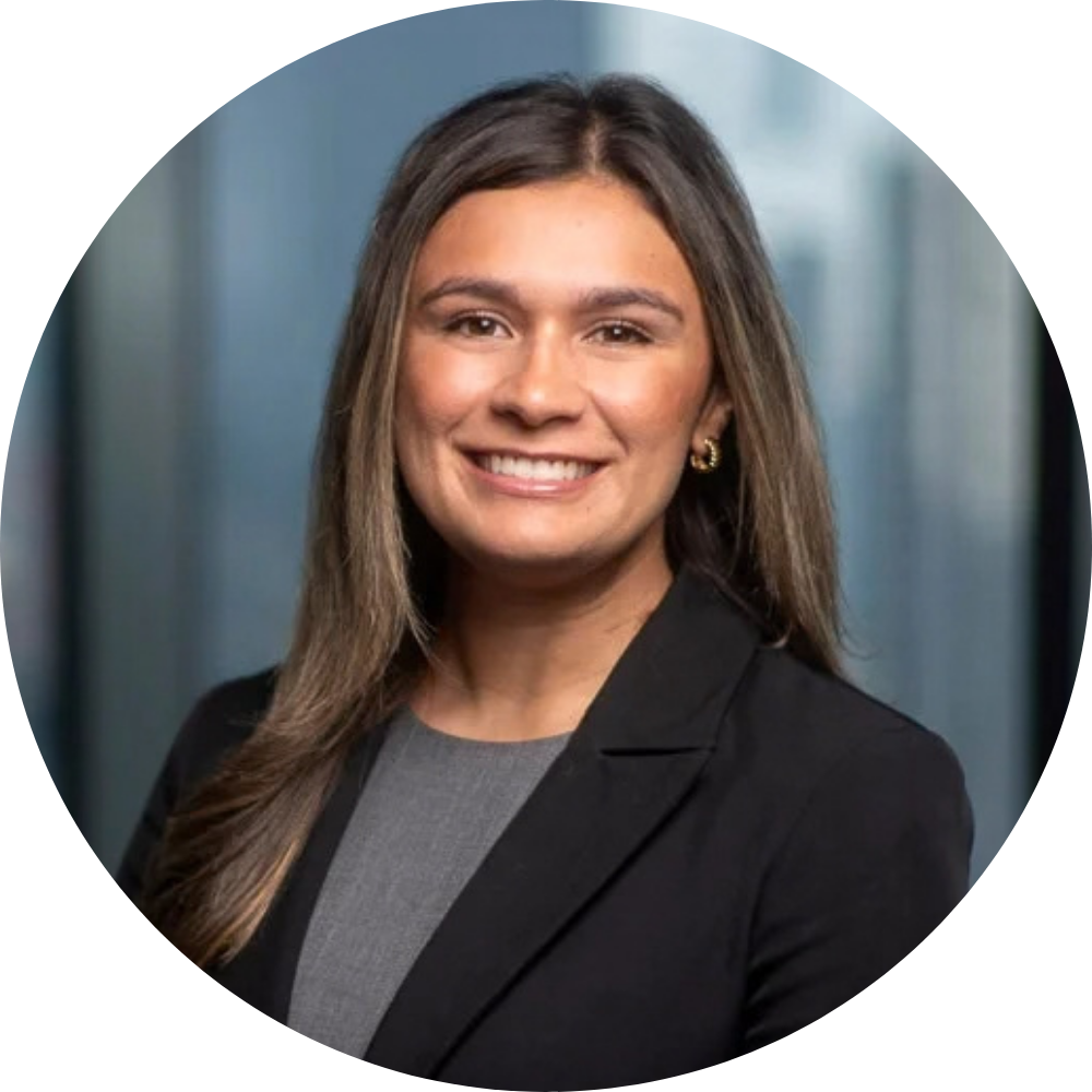Professional headshot of a smiling woman with long straight hair wearing a black blazer and gray top against a blurred office background.