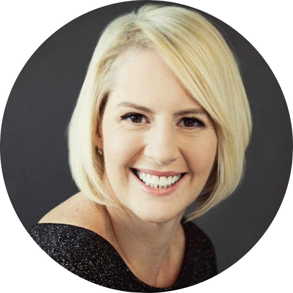 Smiling woman with short blonde hair wearing a black glittery top against a dark gray background.