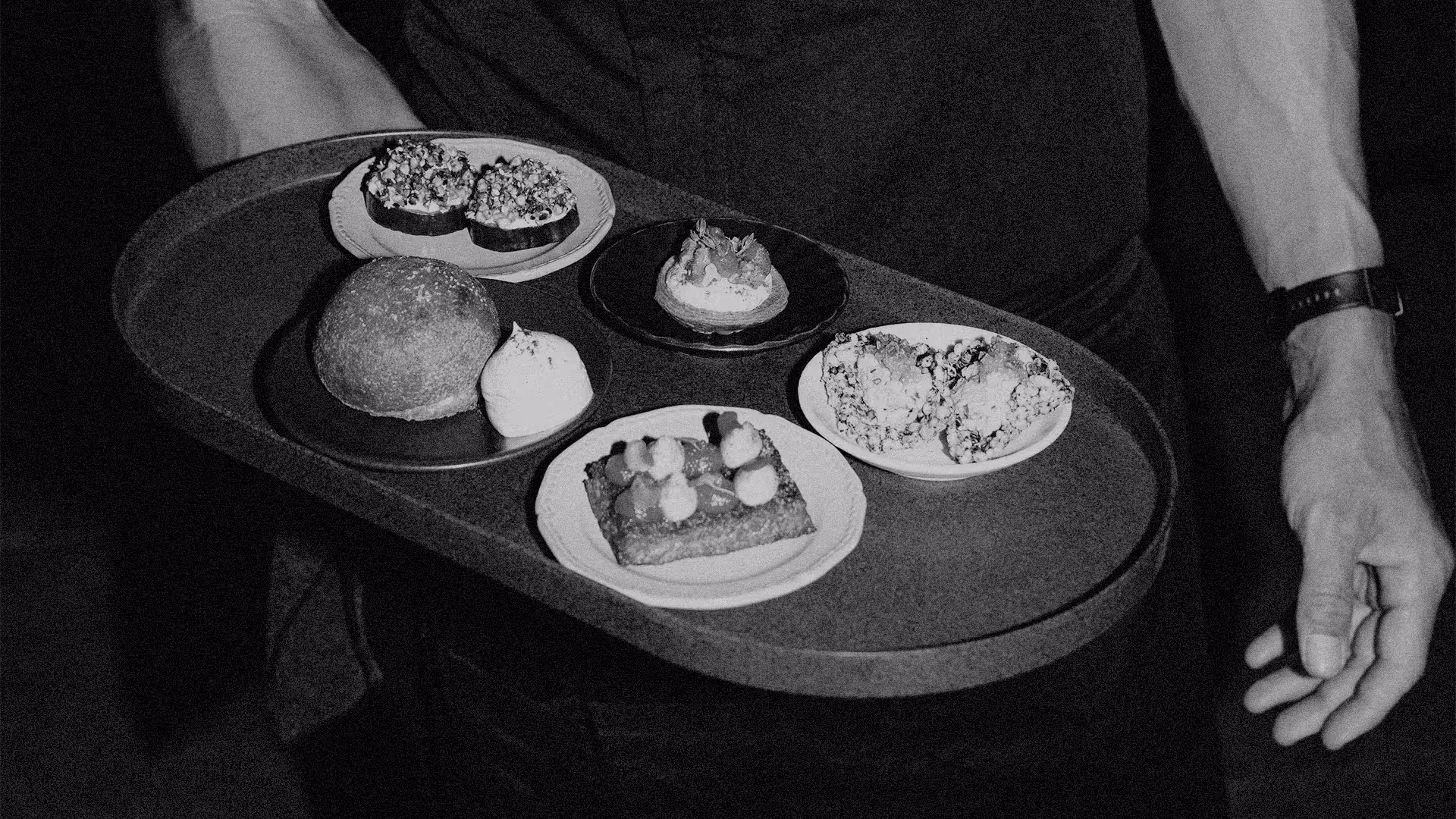 Person holding a tray with five plates of assorted pastries and a dollop of cream.