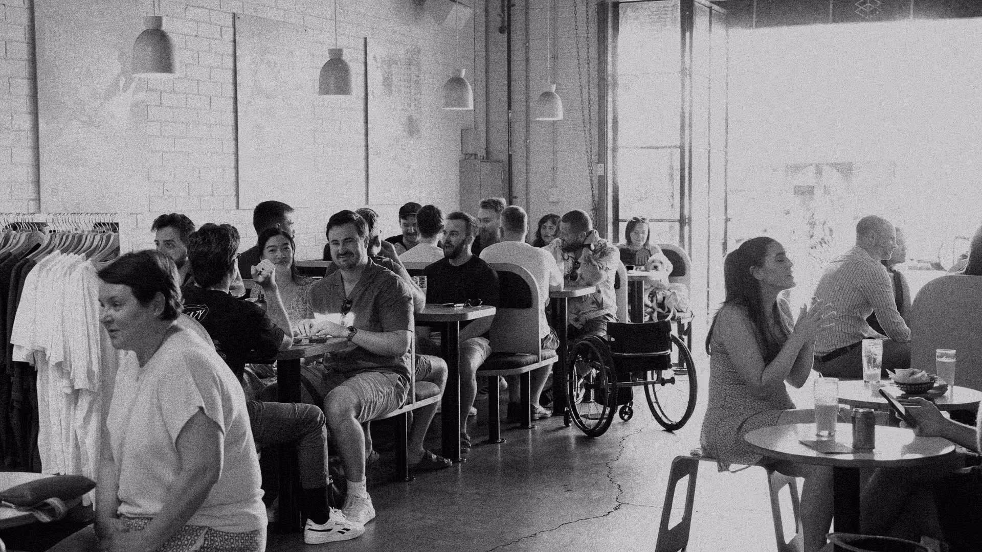 Busy cafe interior with diverse groups of people sitting at tables, engaging in conversation and enjoying drinks, including a person in a wheelchair.