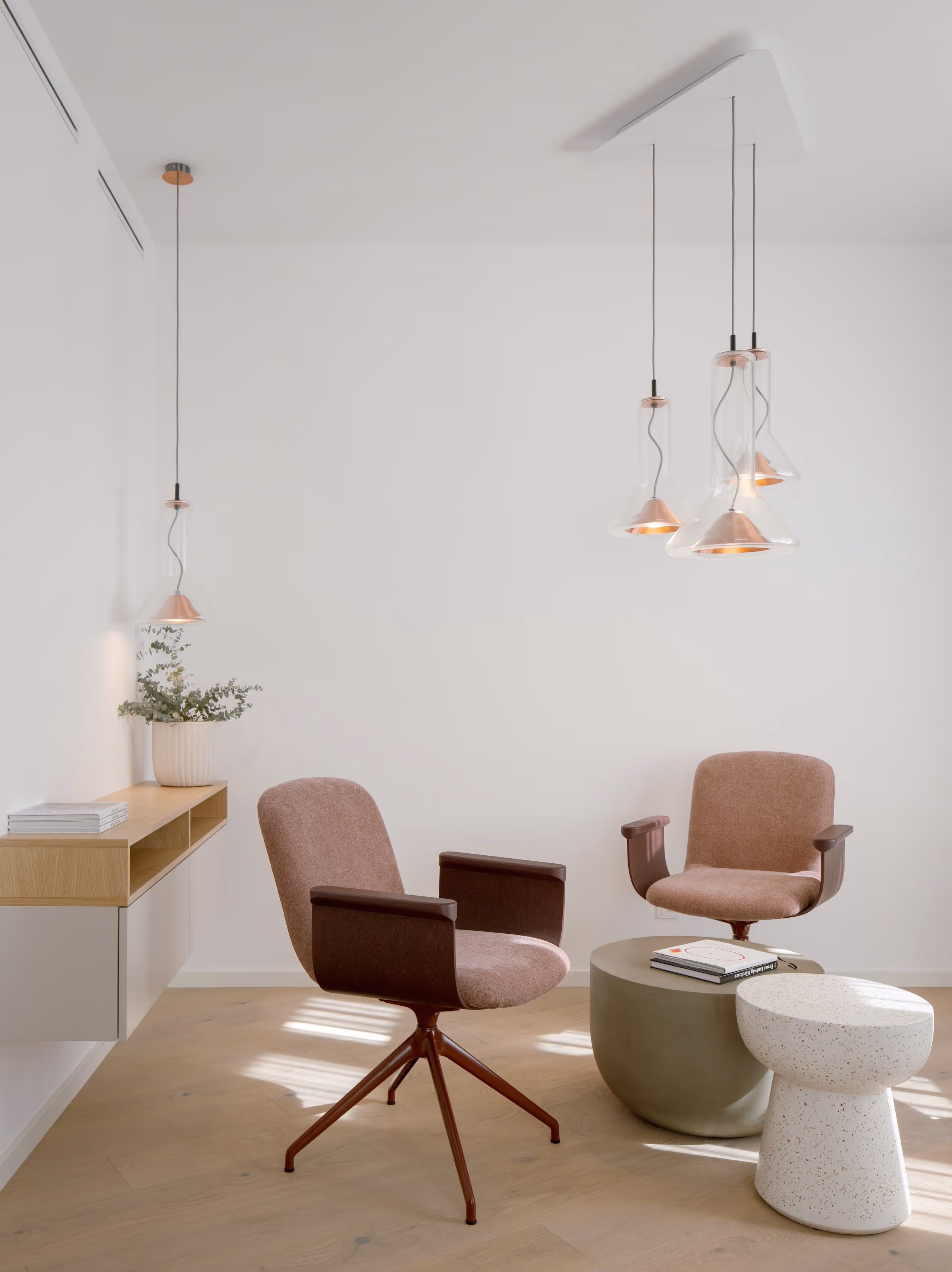 Moderní obývací prostor se dvěma růžovými křesly, kulatým stolkem a závěsnými skleněnými svítidly.