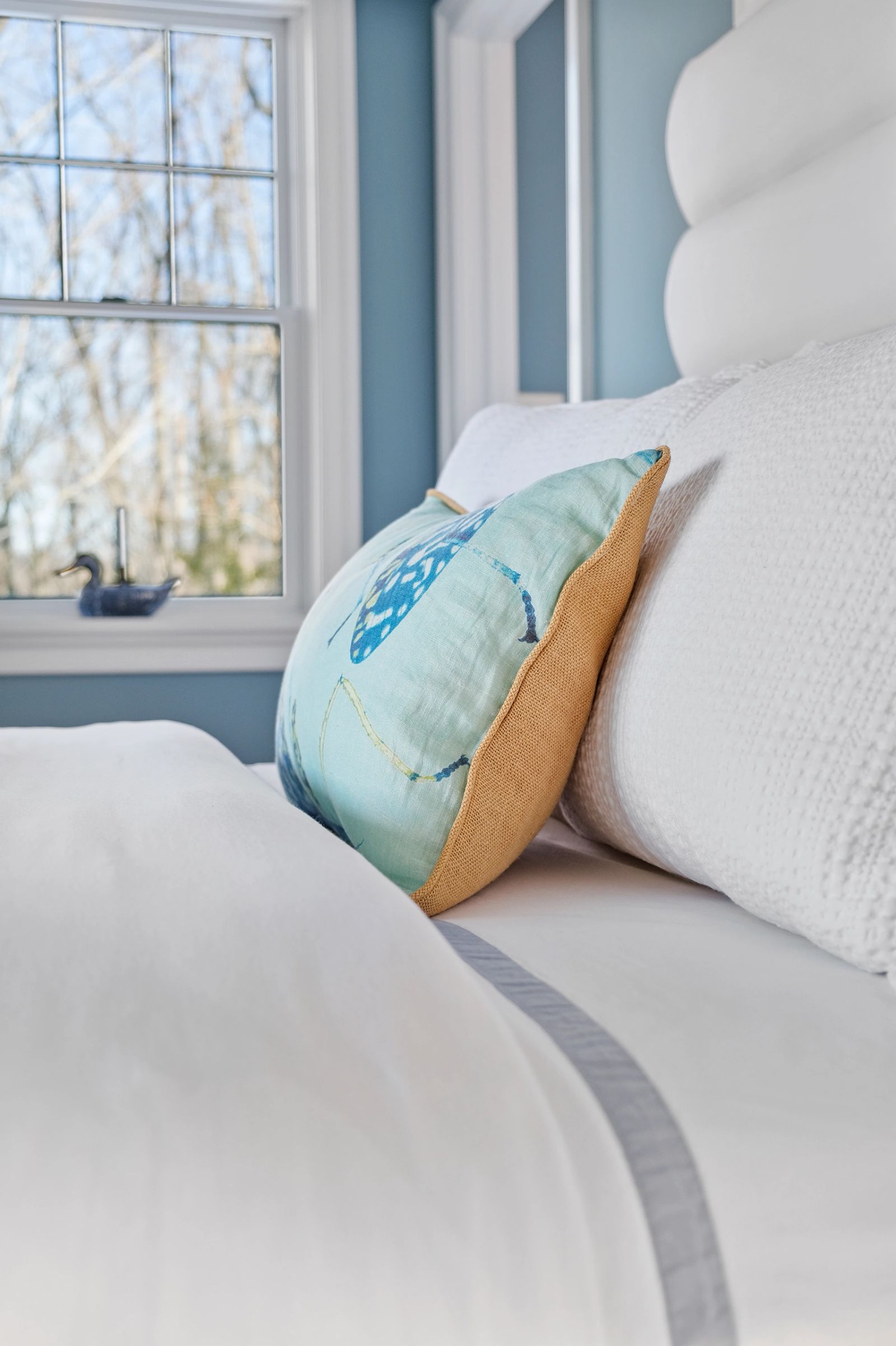 White bedroom with blue cushions and a tall window