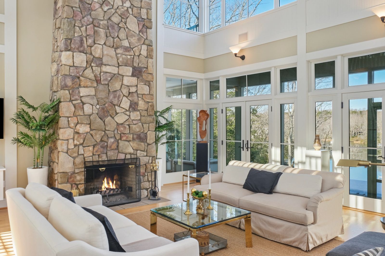 Living room with a stone fireplace, tall glazed walls and neutral seating