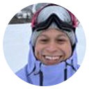 Smiling person wearing ski goggles and a hooded winter jacket in snowy outdoors.