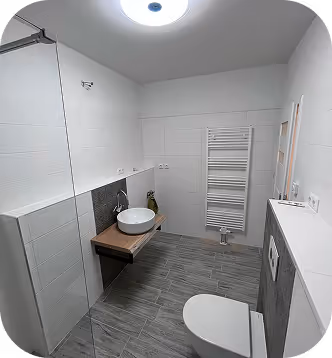 Modern weißes Badezimmer mit einer hängenden Holzablage, rundem Waschbecken, Wandheizkörper und weißer Toilette auf grauen Fliesen.