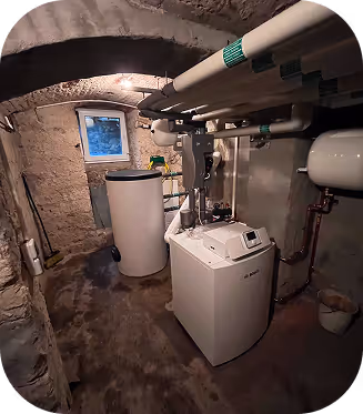 Kellerraum mit Heizungsanlage und Wasseraufbereitung, umgeben von unbehandelten Steinwänden und kleinem Fenster.