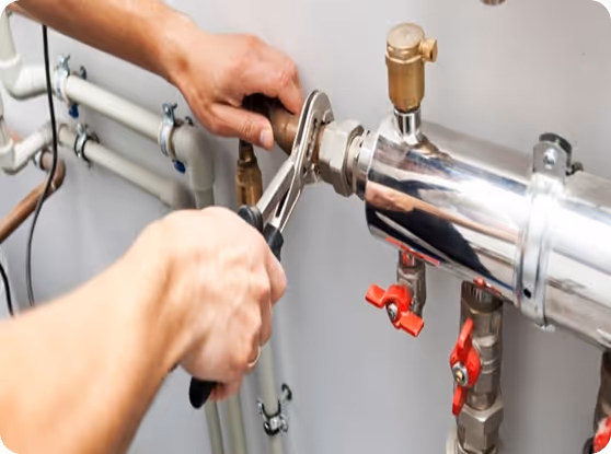 Person benutzt eine Rohrzange, um eine Mutter an einem verchromten Rohr mit roten Ventilgriffen zu befestigen.