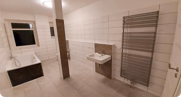 Modernes, weiß gefliestes Badezimmer mit Badewanne, Waschbecken und einem großen Handtuchheizkörper.