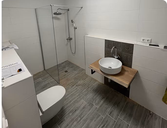 Modernes Badezimmer mit begehbarer Dusche, weißem Wand-WC und rundem Waschbecken auf Holzplatte.