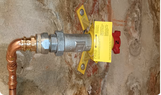 Rohre mit Ventil und gelbem Sicherheitsetikett an einer Steinwand befestigt.