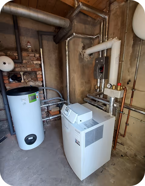 Heizungsanlage mit einem Zylinder-Wasserspeicher und einem Boiler in einem Kellerrraum mit sichtbaren Rohren an den Wänden.