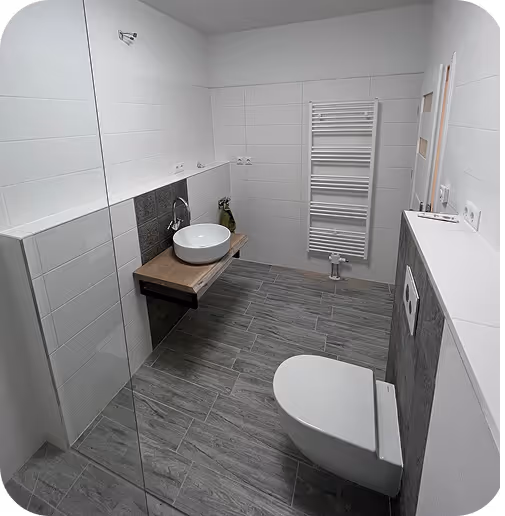 Modernes Badezimmer mit grauen Bodenfliesen, weißem Wand-WC, rundem Waschbecken auf Holzplatte und weißem Handtuchheizkörper.