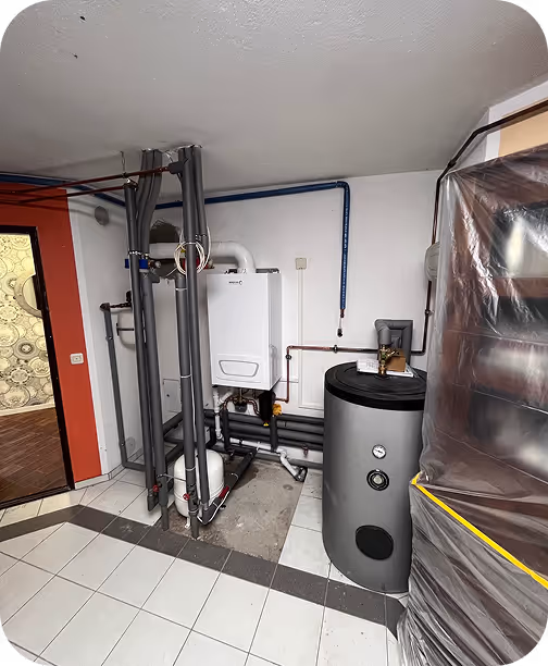 Heizungsanlage mit warmem Wassertank und Rohren in einem Kellerraum mit weiß gekacheltem Boden.
