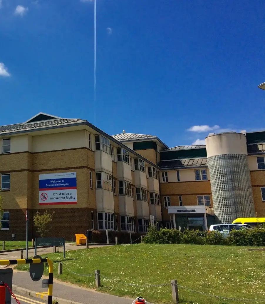 Exterior view of Broomfield Hospital building under blue sky with a sign stating it is a smoke-free facility.